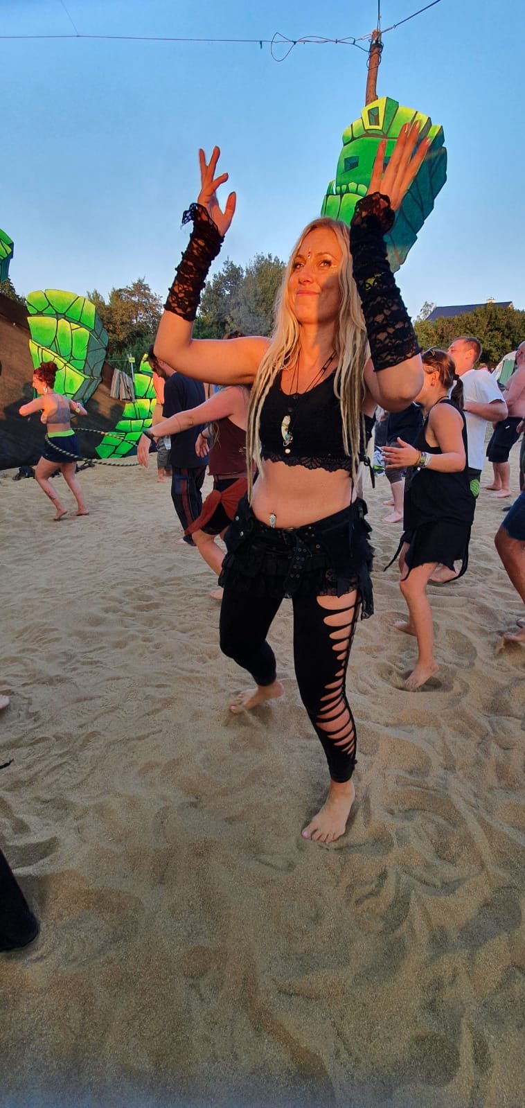 Djane Anastazja dancing barefoot on sand among other dancers at an outdoor festival
