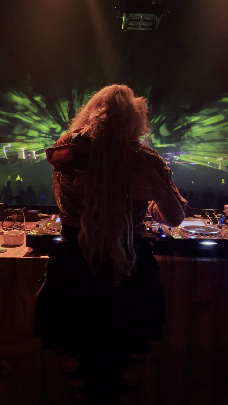 Djane Anastazja seen from behind at the decks, green lasers over the crowd in front of her