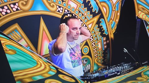 Aurel at the decks, headphones on, in front of a gold and turquoise psychedelic stage backdrop