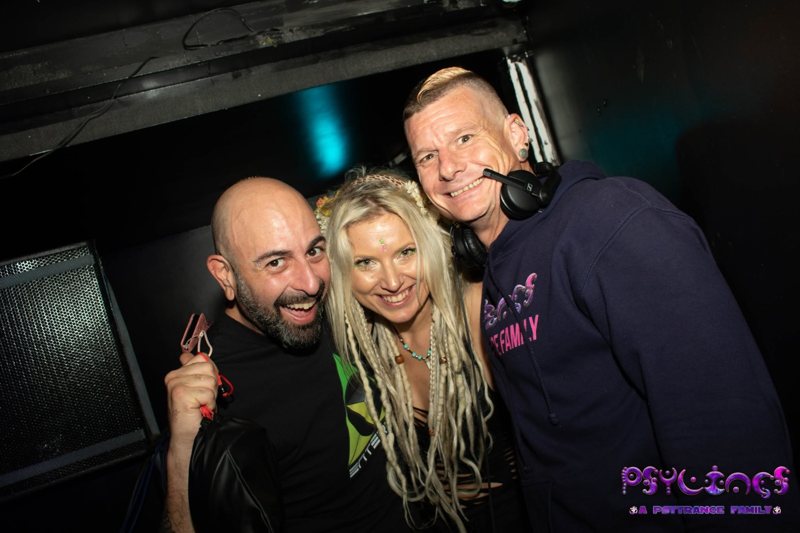 Champa, DJane Anastazja and DJ S&M, arms around each other and smiling by the decks, Sam with headphones round his neck